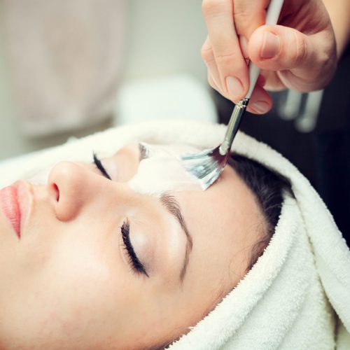 Cosmetician applying facial beauty mask for young beautiful woman at spa salon