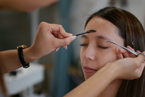 Make up artist shaping eyebrow on female model at studio