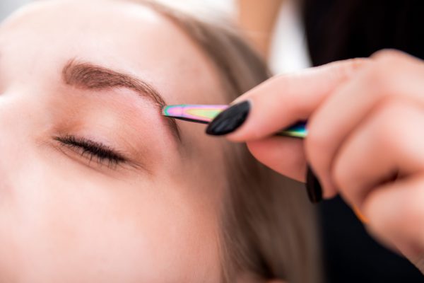 Plucking eyebrows with tweezer by beautician at beauty salon