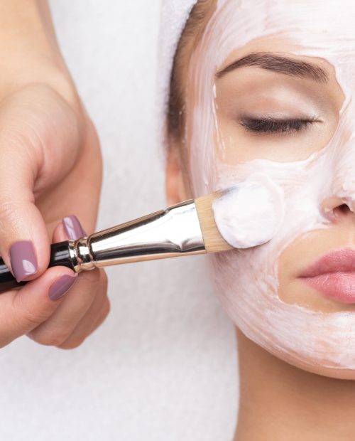 Beautiful young woman receiving facial mask at beauty salon